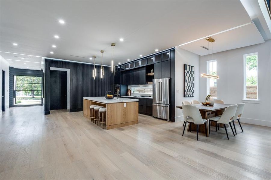 Kitchen featuring high end refrigerator, light hardwood / wood-style floors, pendant lighting, and a kitchen island with sink