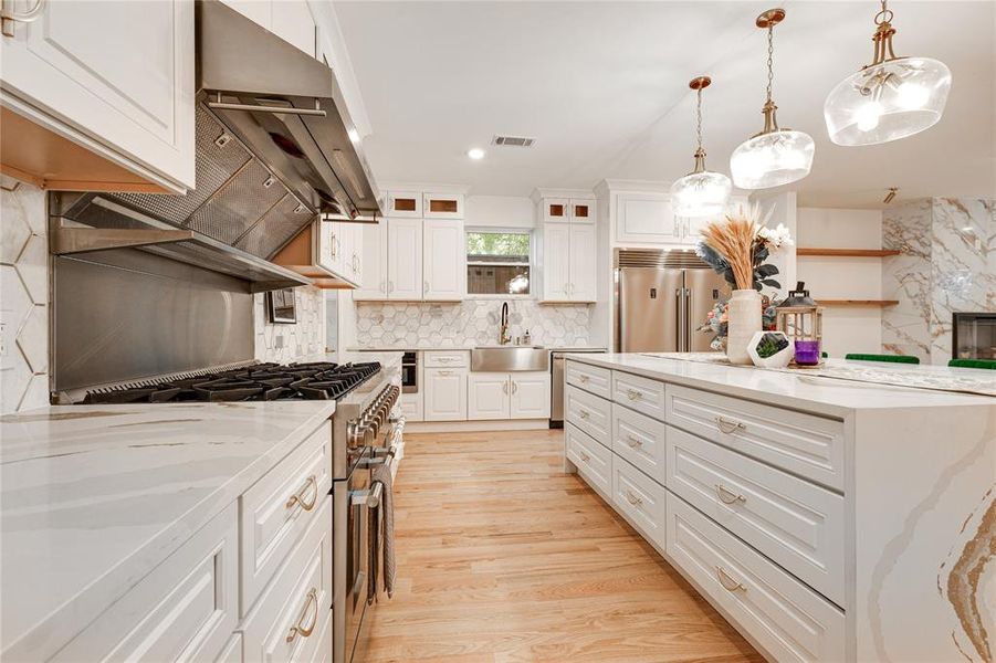 Kitchen with decorative light fixtures, white cabinetry, sink, and high quality appliances