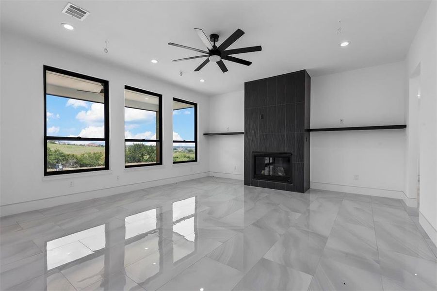 Unfurnished living room with a tiled fireplace, tile walls, ceiling fan, and light tile patterned floors