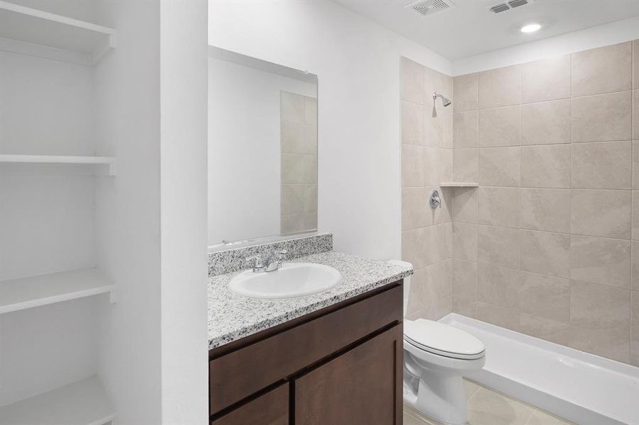 Bathroom with tile patterned flooring, tiled shower, vanity, and toilet