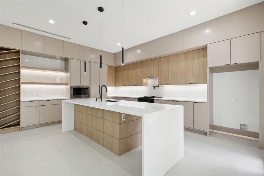 Kitchen with stainless steel microwave, light tile floors, hanging light fixtures, sink, and a kitchen island with sink