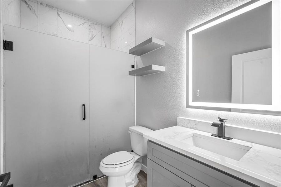 Bathroom featuring hardwood / wood-style flooring, vanity, toilet, and tiled shower