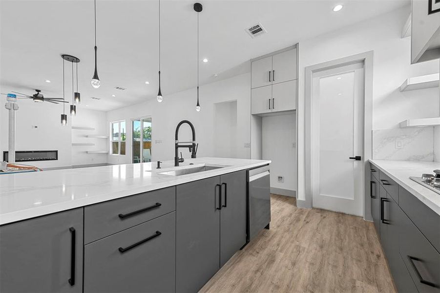 Kitchen with sink, light wood-type flooring, hanging light fixtures, and gray cabinetry
