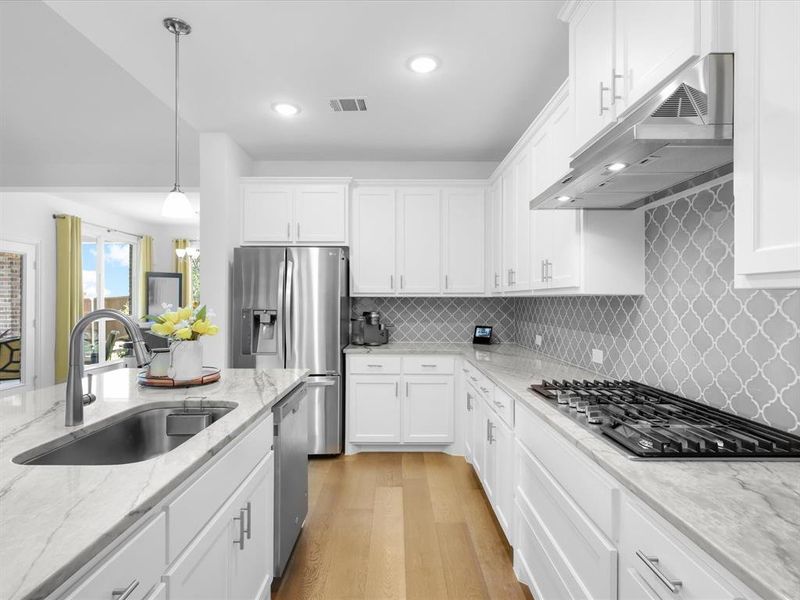 Kitchen featuring light hardwood / wood-style flooring, stainless steel appliances, sink, backsplash, and decorative light fixtures