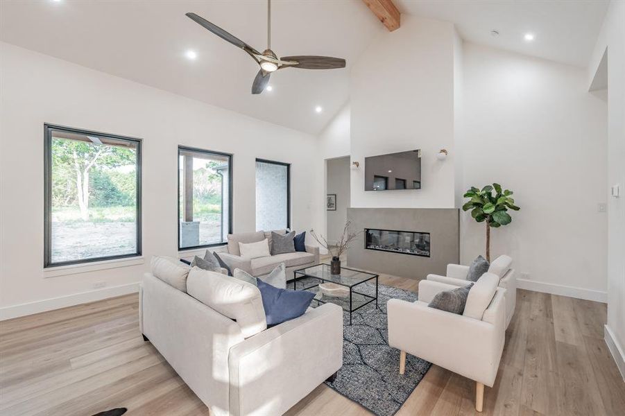 Living room featuring high vaulted ceiling, beam ceiling, ceiling fan, and blonde plank, wood-like luxury vinyl floors.