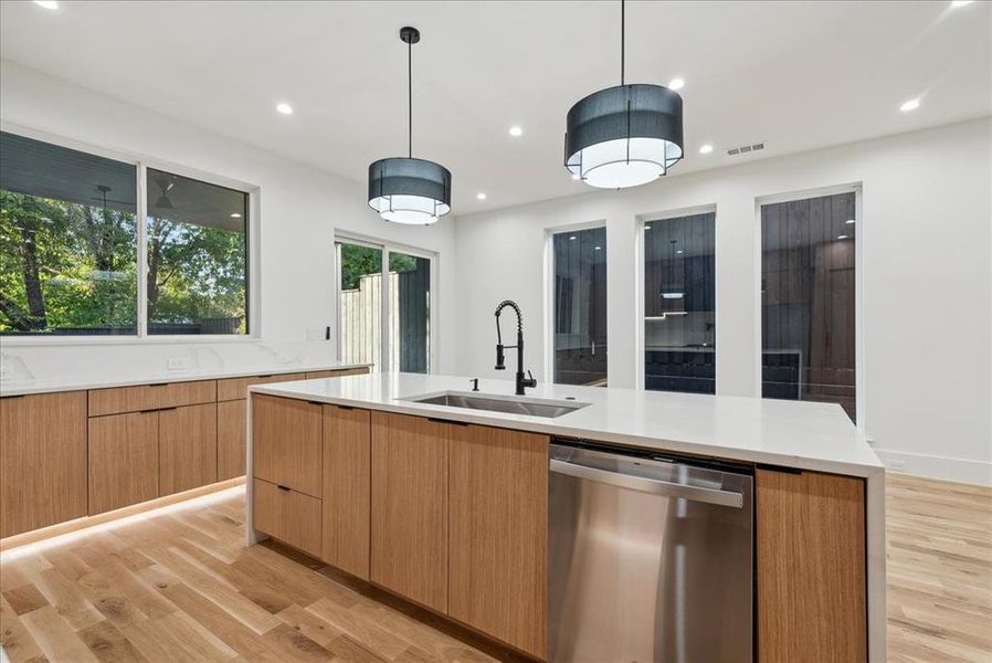 Kitchen with an island with sink, light wood-type flooring, sink, pendant lighting, and dishwasher