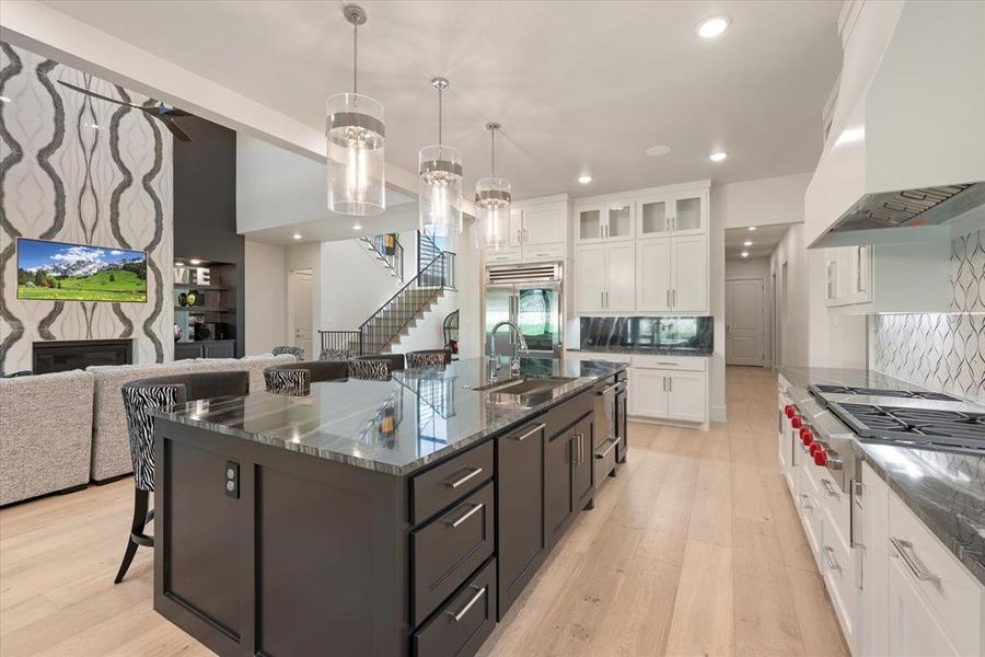 Kitchen with white cabinets, a high end fireplace, custom exhaust hood, light hardwood / wood-style floors, and an island with sink