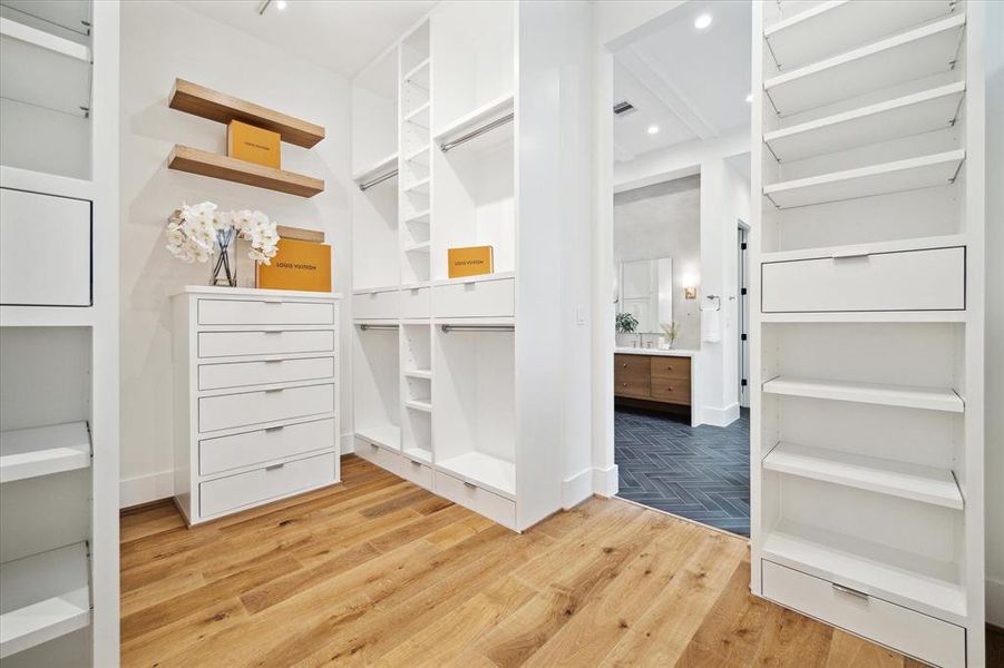 The large walk-in closet features custom built-ins, three levels of hanging space, open shelving, and drawers, offering ample storage solutions. Enhanced with WAC track lighting, the closet ensures efficient organization and easy access to wardrobe essentials.