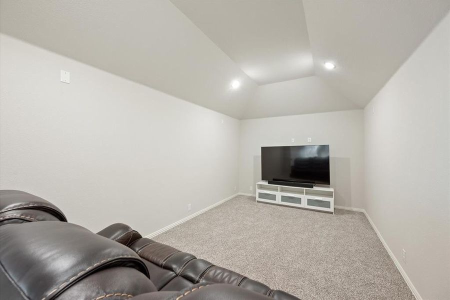 Fantastic media room has stadium seating, a vaulted ceiling, recessed canned lighting and carpet flooring.