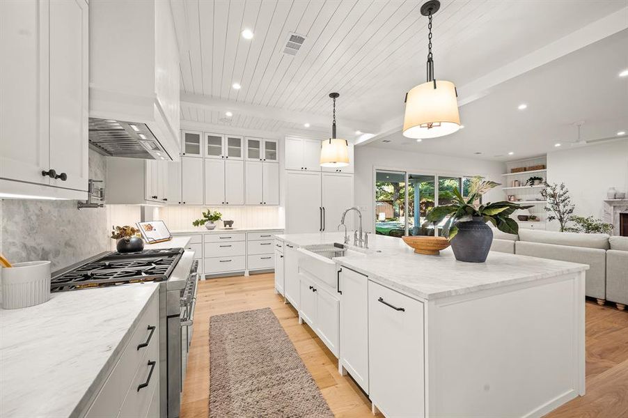 Kitchen with an island with sink, hanging light fixtures, light hardwood / wood-style flooring, white cabinetry, and stainless steel stove