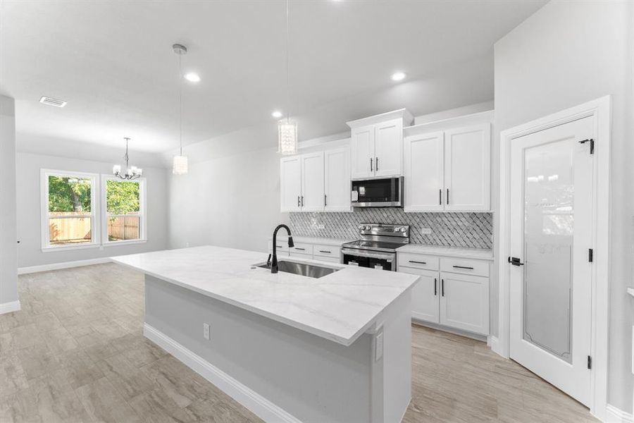 Kitchen with pendant lighting, sink, white cabinets, stainless steel appliances, and a center island with sink