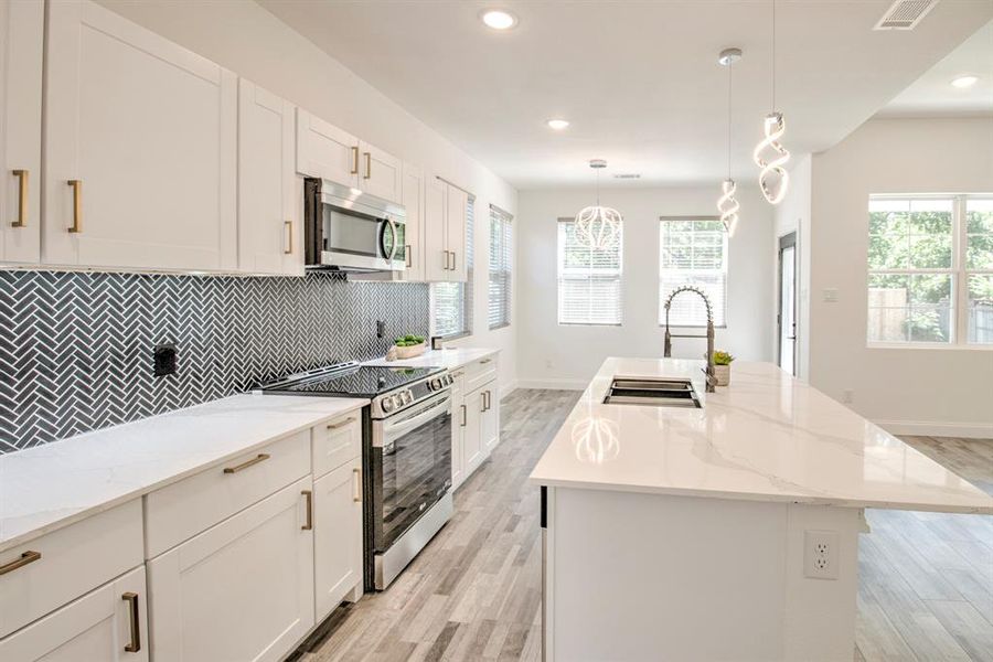Kitchen with a center island with sink, white cabinets, stainless steel appliances, decorative light fixtures, and sink