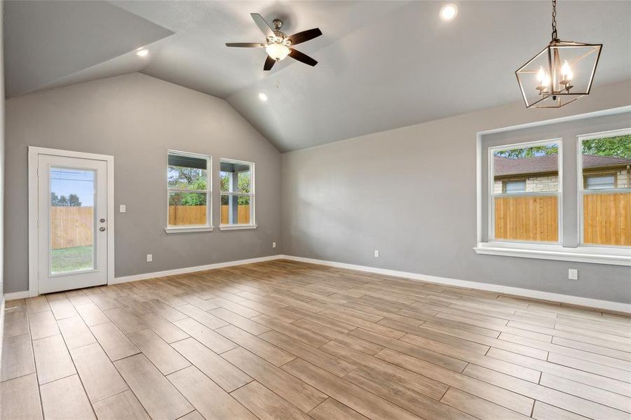 Spare room featuring a healthy amount of sunlight, vaulted ceiling, ceiling fan with notable chandelier, and light hardwood / wood-style flooring