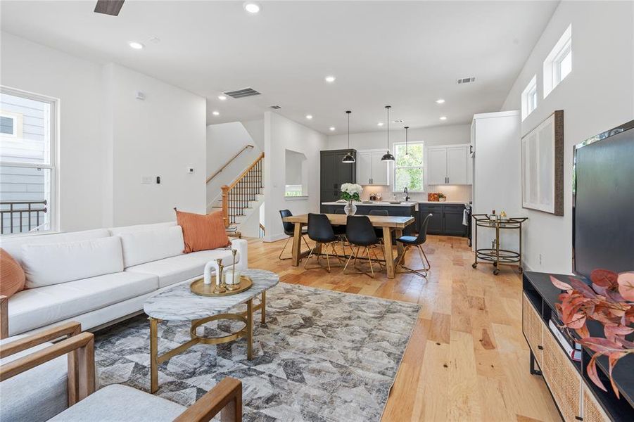 From a strategic corner vantage point, the open-concept living, dining, and kitchen areas seamlessly flow together, as the stairway invites exploration, all unified by the warm, rich hues of engineered wood flooring throughout the home.