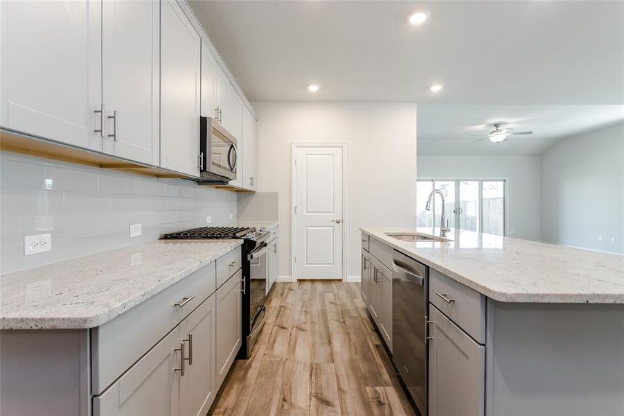 Kitchen with light wood-type flooring, appliances with stainless steel finishes, sink, and an island with sink