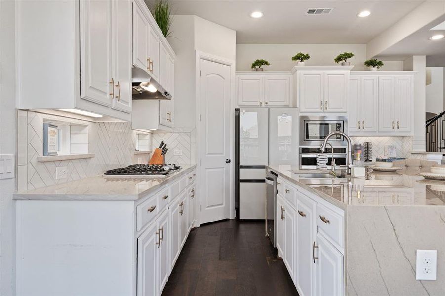 Kitchen featuring dark hardwood / wood-style floors, tasteful backsplash, stainless steel appliances, a center island with sink, and white cabinetry
