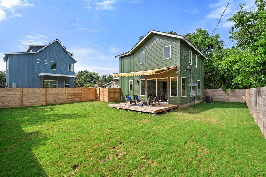 Rear view of property with a wooden deck, a lawn, and cooling unit
