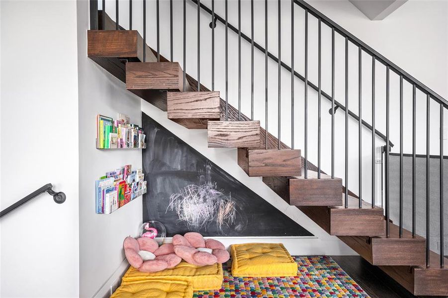 This stylish staircase leads to the third floor and features a sleek custom stair railing that adds a modern touch to the space. Below the stairs, a cozy nook creates a perfect reading or play area, complete with cushions and built-in bookshelves.