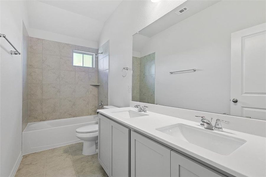 Full bathroom featuring dual sinks, tile flooring, vanity with extensive cabinet space, tiled shower / bath combo, and toilet