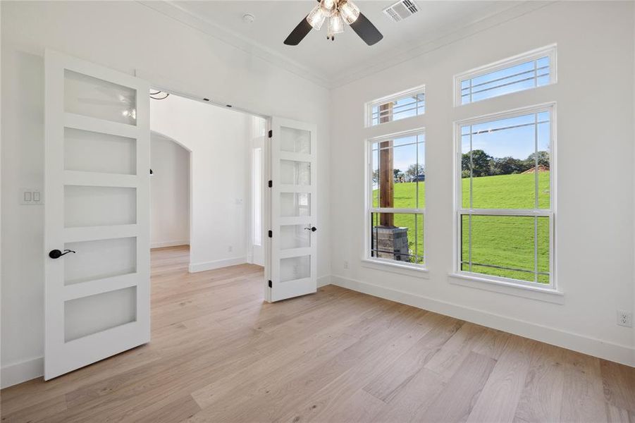 Empty room featuring light hardwood / wood-style floors, ceiling fan, built in shelves, and ornamental molding