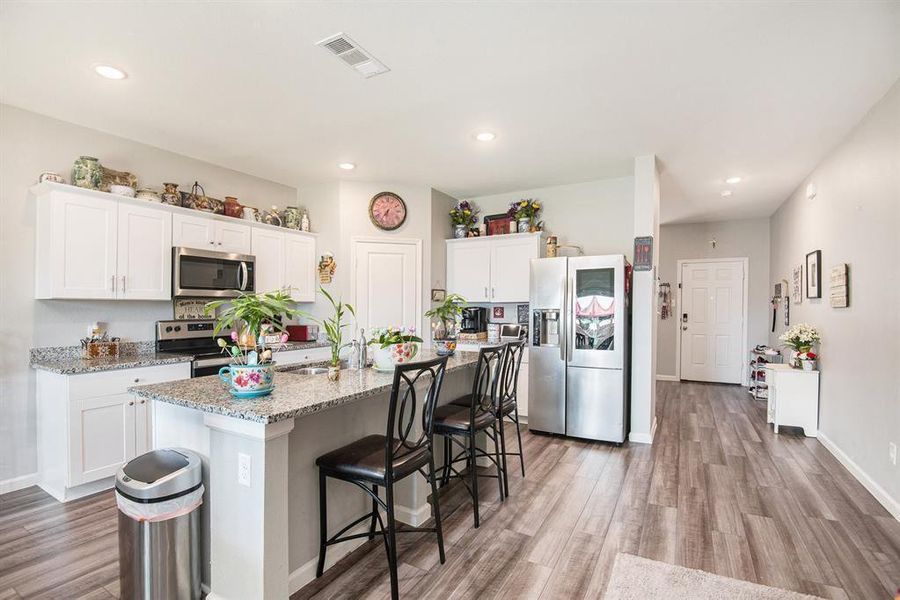 Kitchen featuring hardwood / wood-style flooring, stainless steel appliances, white cabinets, and a center island with sink