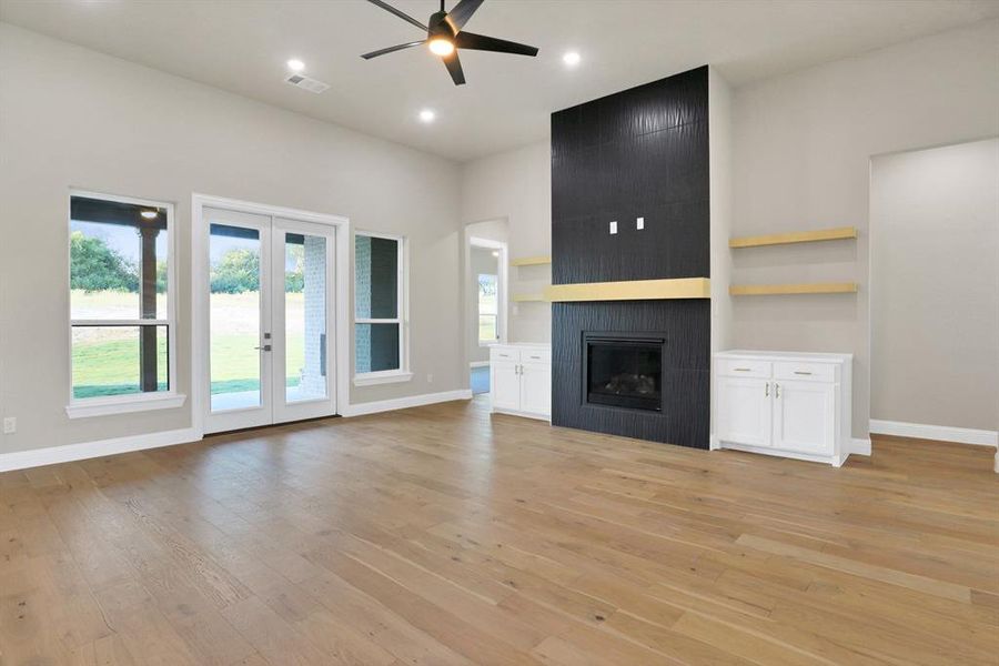 Unfurnished living room with french doors, ceiling fan, a large fireplace, and light hardwood / wood-style flooring