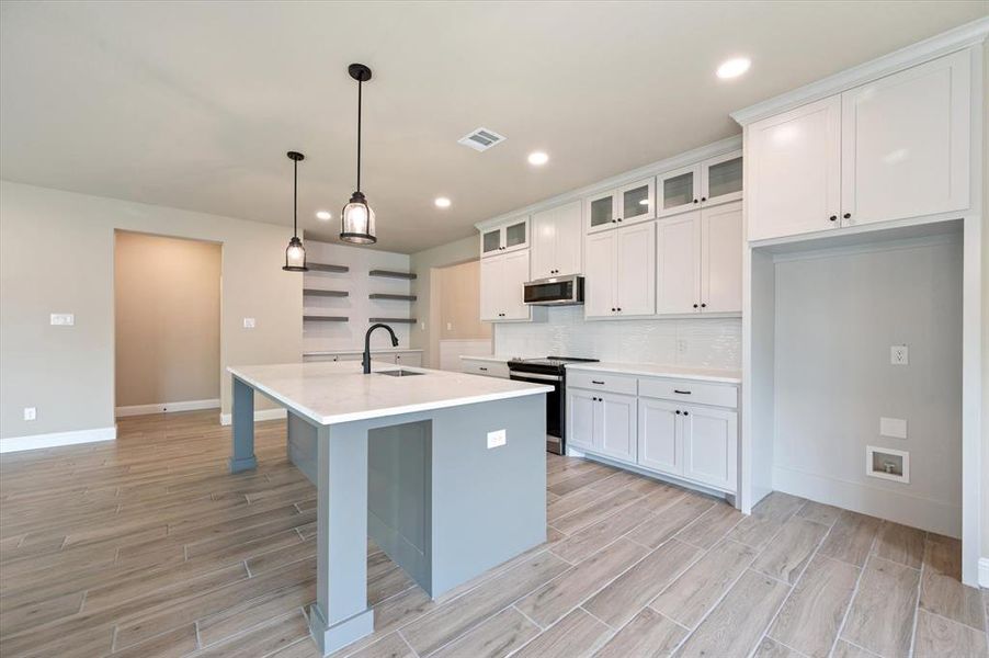 Kitchen featuring decorative backsplash, white cabinets, a center island with sink, and stainless steel appliances