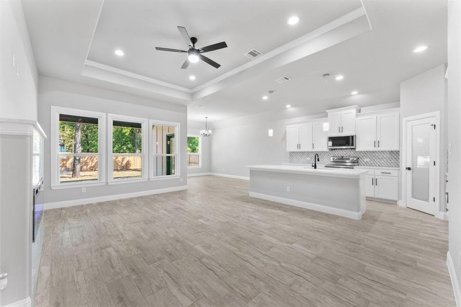 Kitchen featuring a tray ceiling, light hardwood / wood-style floors, an island with sink, white cabinets, and appliances with stainless steel finishes