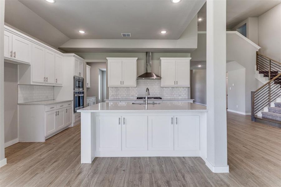 Kitchen featuring wall chimney range hood, light hardwood / wood-style flooring, stainless steel appliances, and white cabinets