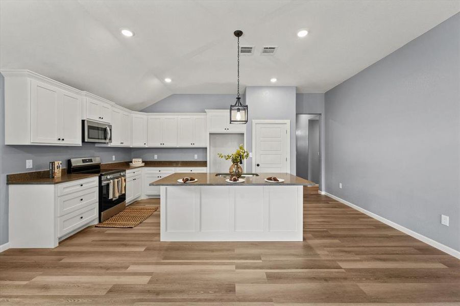 Kitchen featuring stainless steel appliances, white cabinetry, light hardwood / wood-style flooring, and a kitchen island with sink