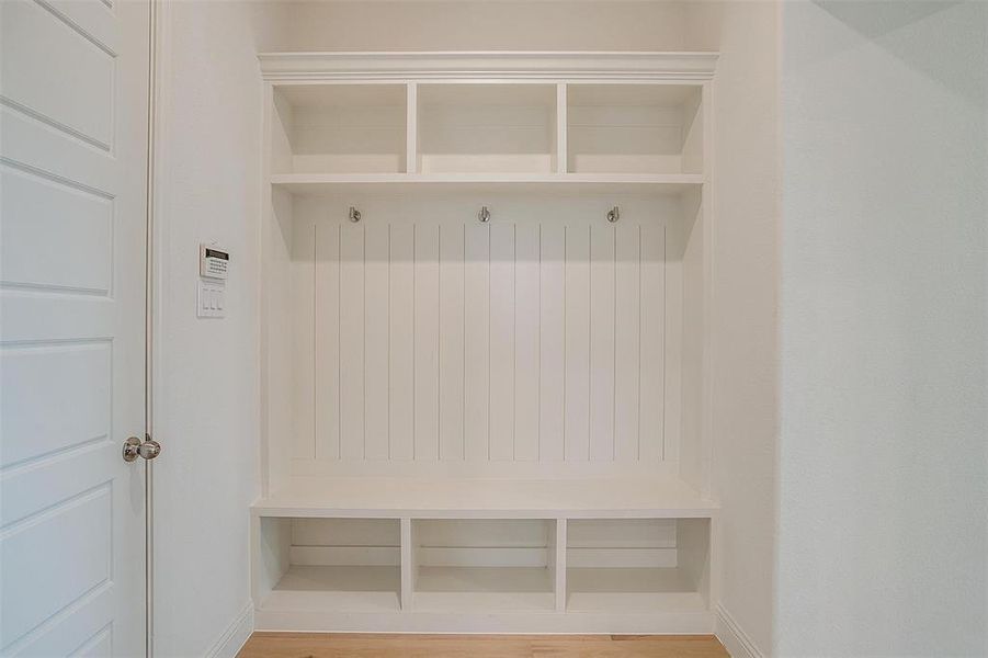 Mudroom with light wood-type flooring and custom mud-bench with hooks.