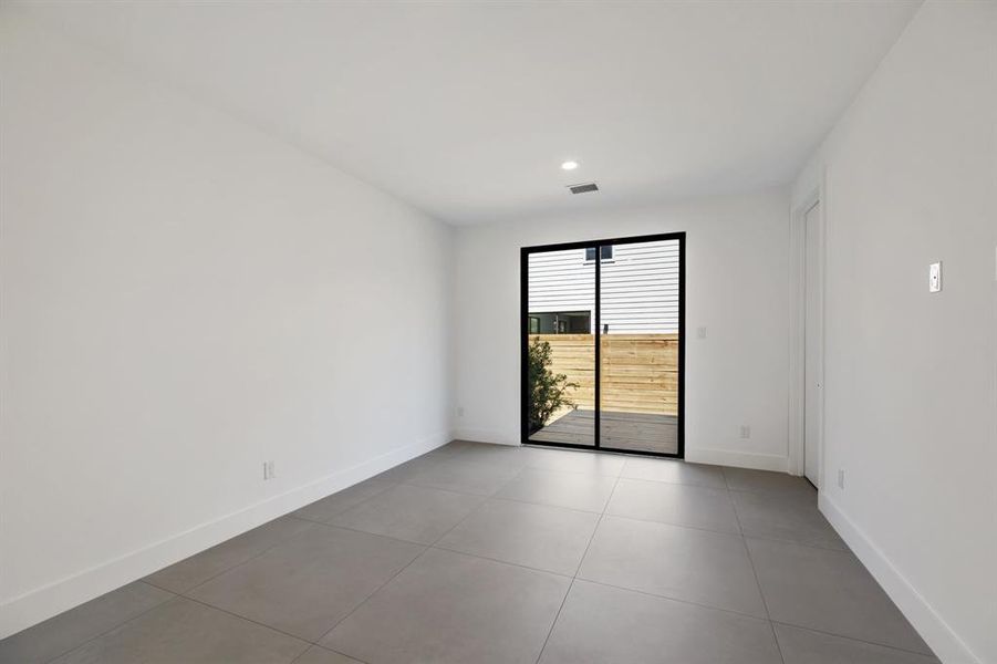 This is a modern, minimalistic room featuring white walls, and a black-framed glass door leading to an outdoor wooden deck. It offers ample natural light and a clean design, ready for personalization.