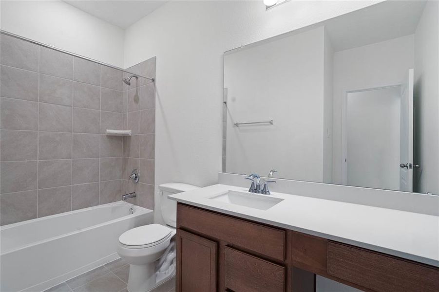 Secondary bath features tile flooring, tub/shower combo with tile surround, stained wood cabinets, beautiful light countertops, mirror, sleek fixtures and modern finishes.