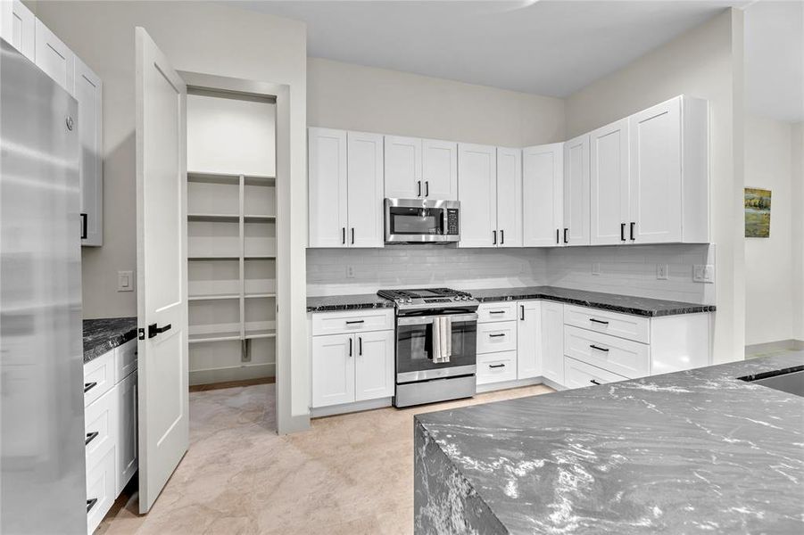 Walk in pantry, white cabinets, stainless steel refrigerator, granite counter tops with stylish light fixtures