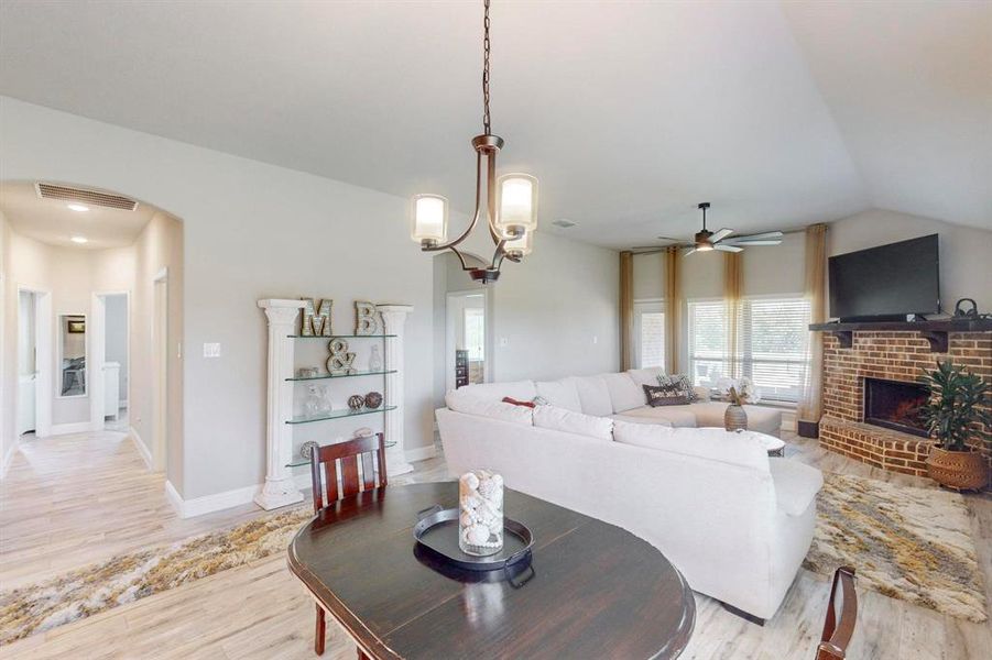 Living room with a fireplace, ceiling fan with notable chandelier, lofted ceiling, and light wood-type flooring