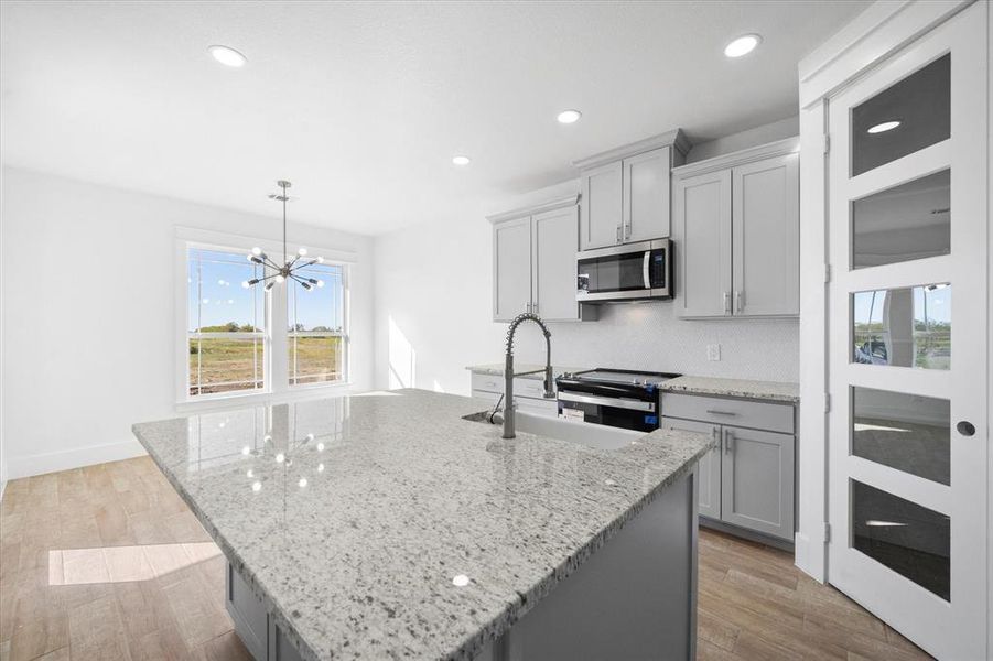 Kitchen with gray cabinetry, light hardwood / wood-style floors, stainless steel appliances, and a center island with sink