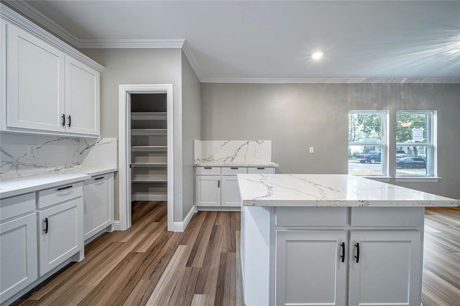 Kitchen featuring light stone countertops, wood-type flooring, a kitchen island, white cabinets, and ornamental molding