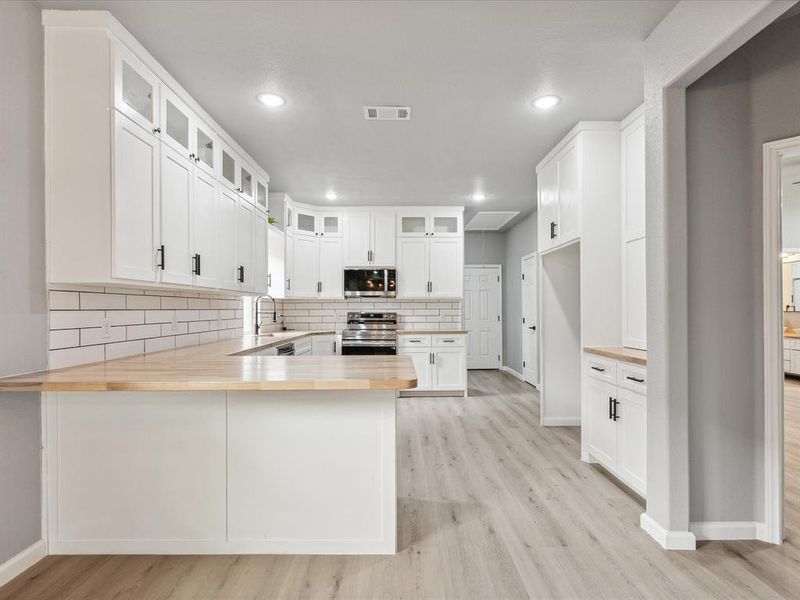 Kitchen with stainless steel appliances, tasteful backsplash, kitchen peninsula, and light hardwood / wood-style floors