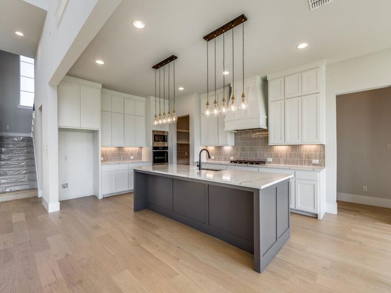 Kitchen featuring a large island with sink, stainless steel appliances, white cabinets, custom range hood, and light hardwood / wood-style floors