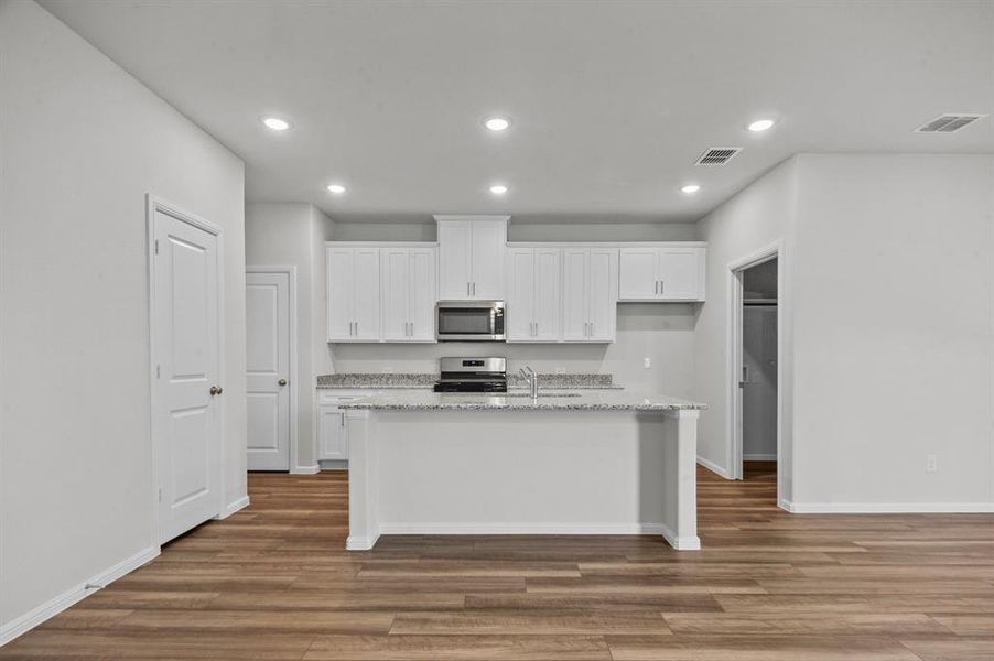 Kitchen featuring dark wood-type flooring, appliances with stainless steel finishes, a kitchen island with sink, and white cabinets