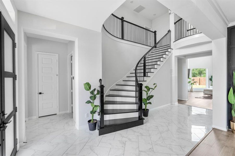 The entryway has chevron tile floors adding texture to the floor, impressive high ceilings, and a beautiful staircase with the trademark black accents on white that you see from Newmark design.