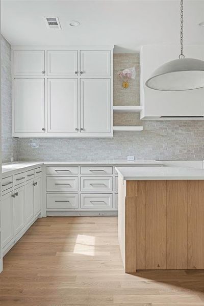 Kitchen featuring white cabinets, pendant lighting, decorative backsplash, and light hardwood / wood-style floors