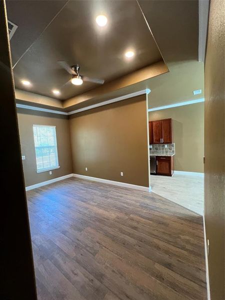 Empty room with ceiling fan, wood-type flooring, and a raised ceiling