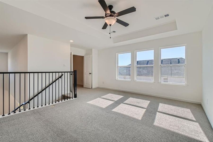 Carpeted empty room featuring ceiling fan and a tray ceiling