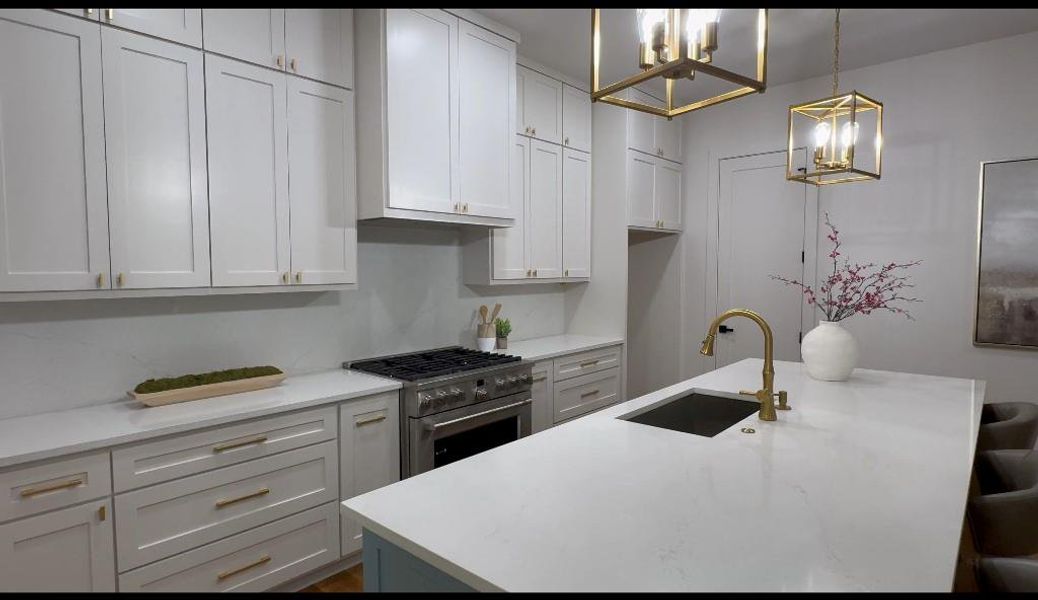 Kitchen featuring stainless steel range, a breakfast bar area, sink, decorative light fixtures, and a center island with sink
