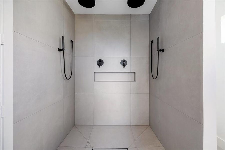 This is a modern walk-in shower with sleek gray tiles, featuring dual black showerheads and a minimalist design.