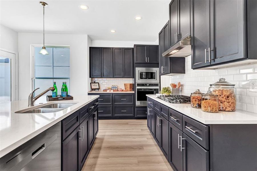 Kitchen with decorative light fixtures, stainless steel appliances, decorative backsplash, sink, and light hardwood / wood-style floors
