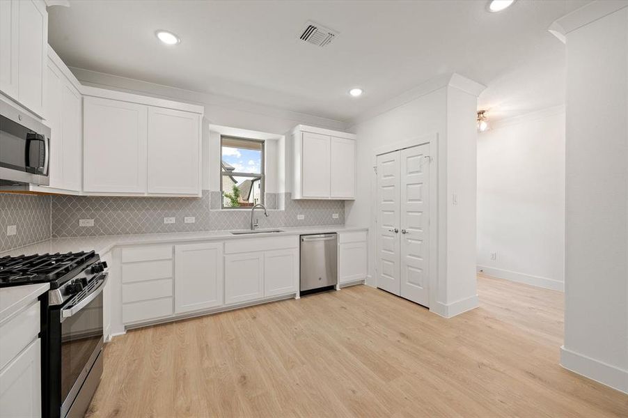 Kitchen featuring white cabinets, stainless steel appliances, sink, and light wood-type flooring