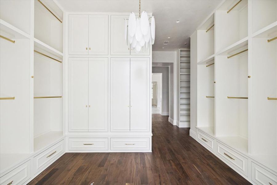 The primary suite features very spacious dual closets. The closet features several hanging racks, built-in shelving, cabinets, and drawers along with a stylish chandelier.