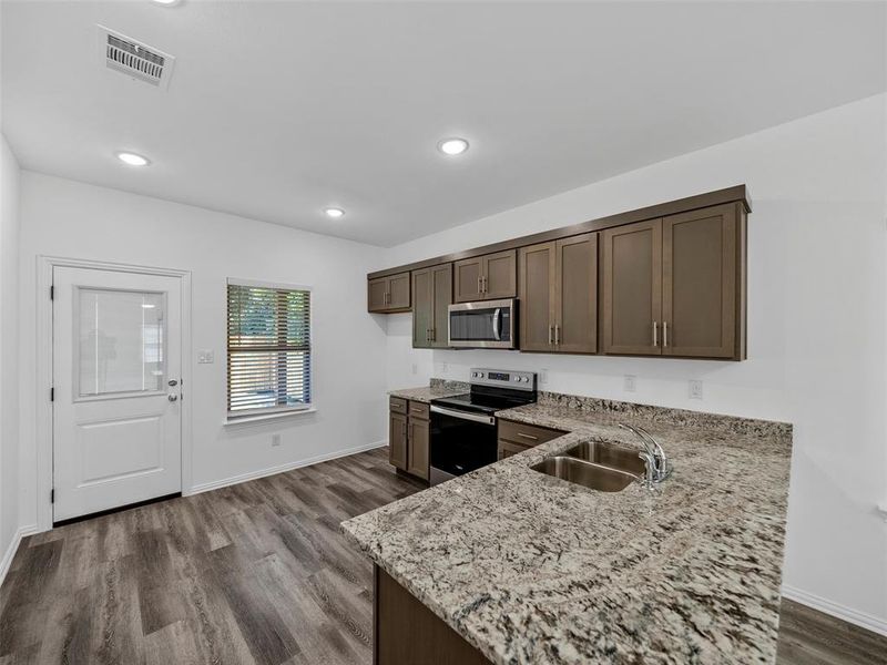 Kitchen with sink, light stone countertops, dark brown cabinetry, appliances with stainless steel finishes, and dark hardwood / wood-style flooring